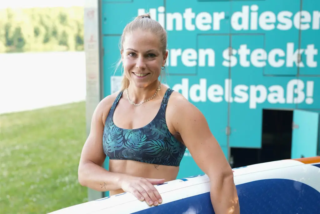 Frau mit SUP-Board vor Beschilderung am Otto-Maigler-See