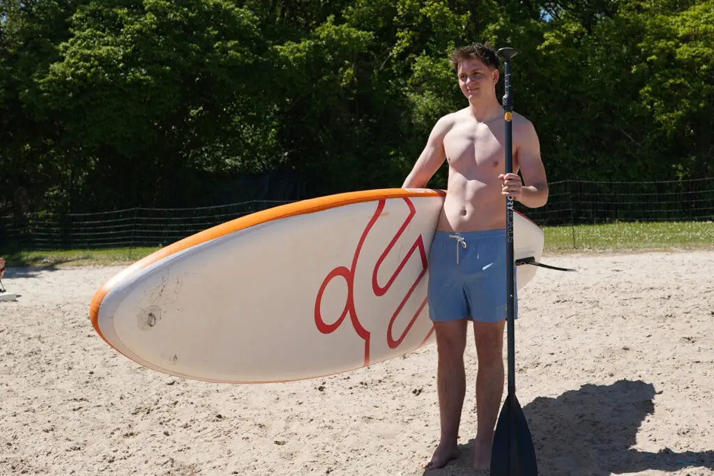 Mann trägt ein SUP-Board am Strand des Otto-Maigler-Sees