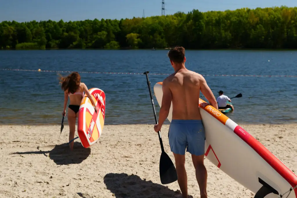 Zwei Personen mit SUP-Boards am Strand des Otto-Maigler-Sees