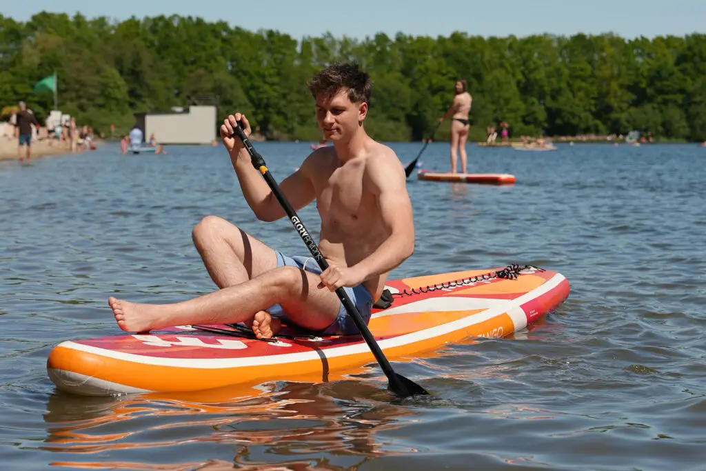Mann sitzt auf einem SUP-Board und paddelt über den See